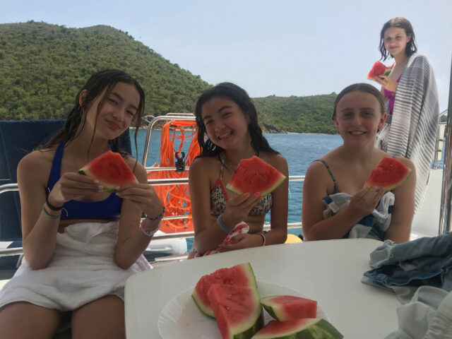 Three girls eating watermelon on a boat.
