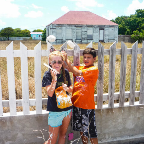 Two campers having fun together painting a fence.