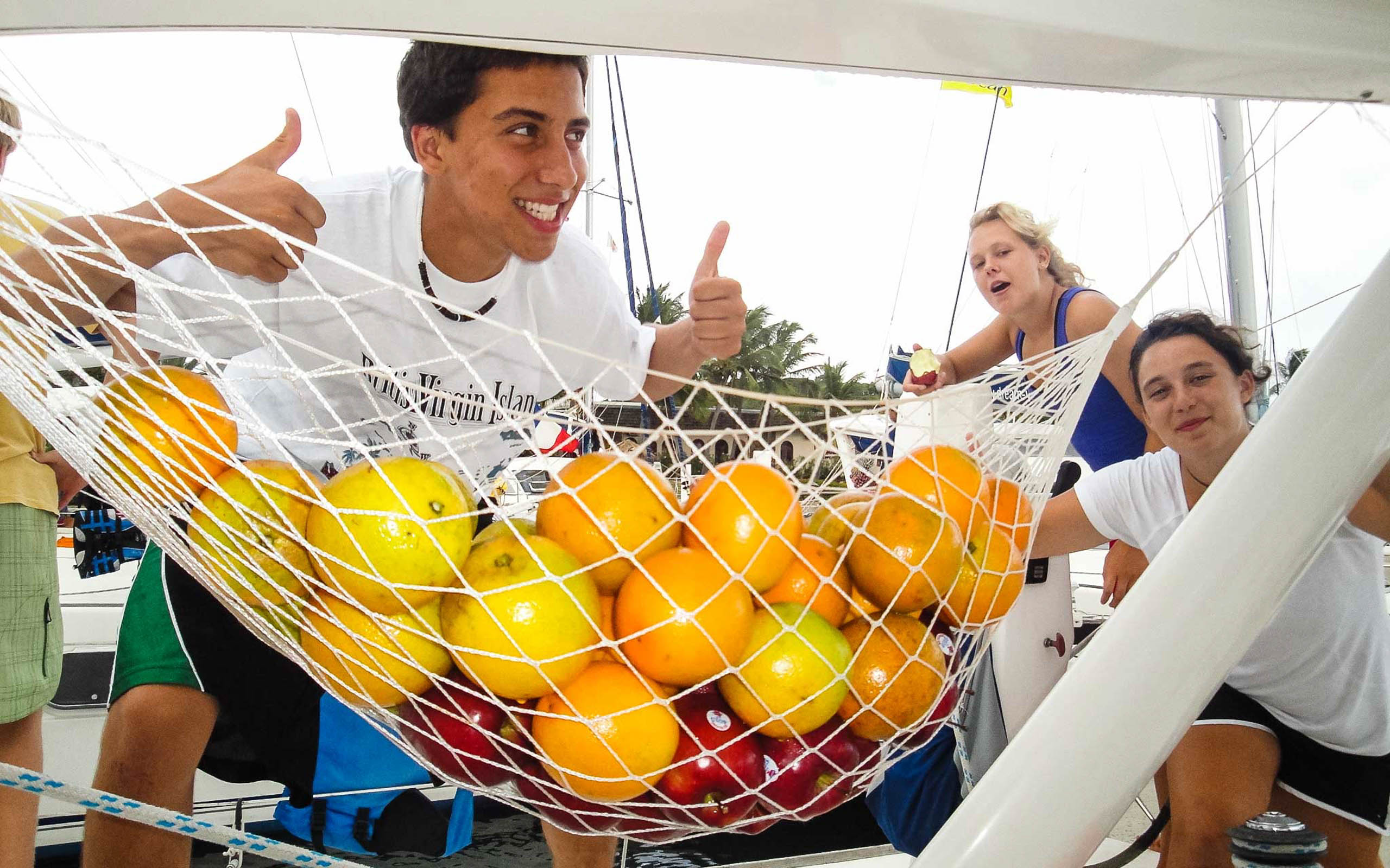 A group of people on a sailboat with oranges in a net.