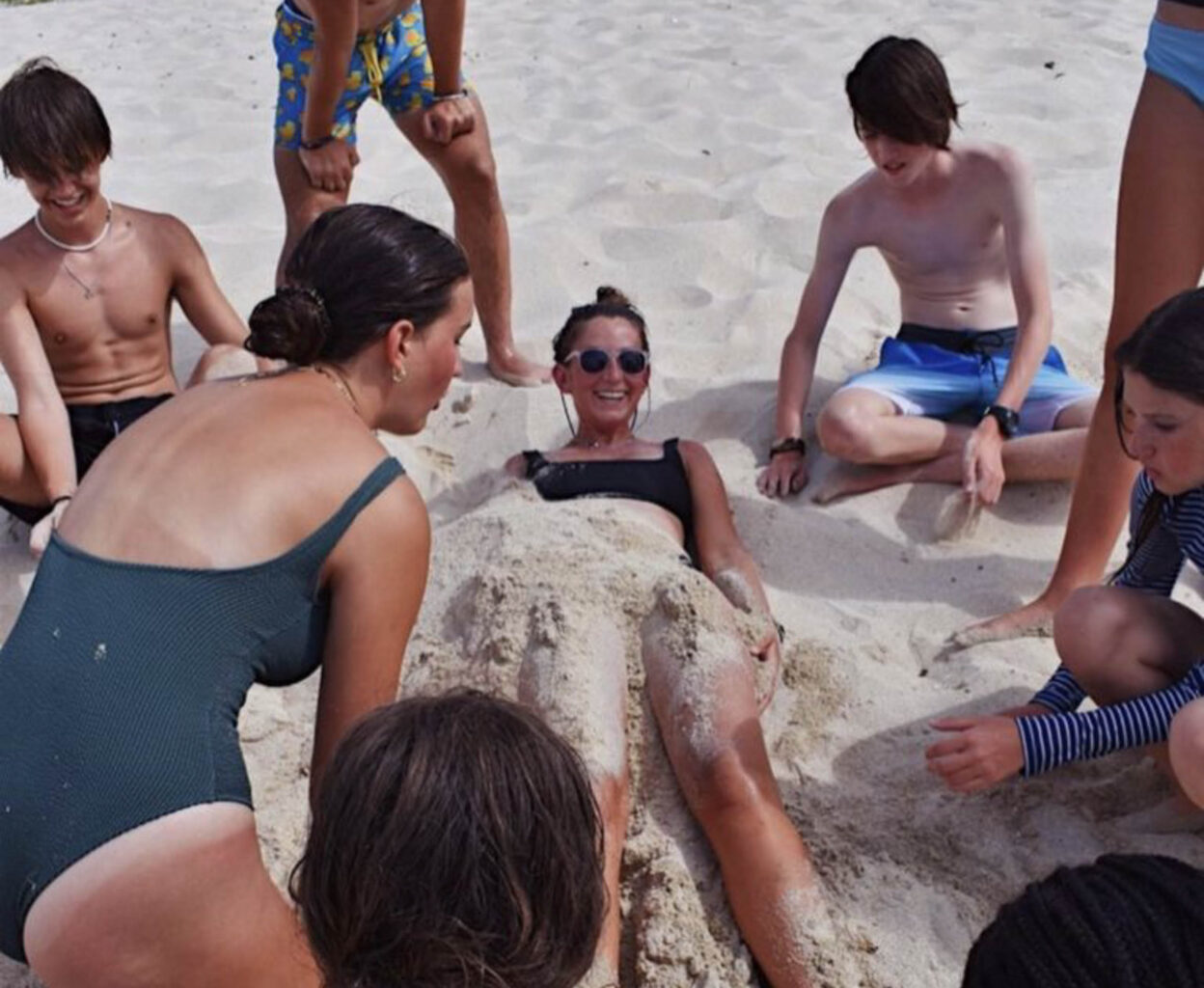 Campers burying a staff member in the sand.