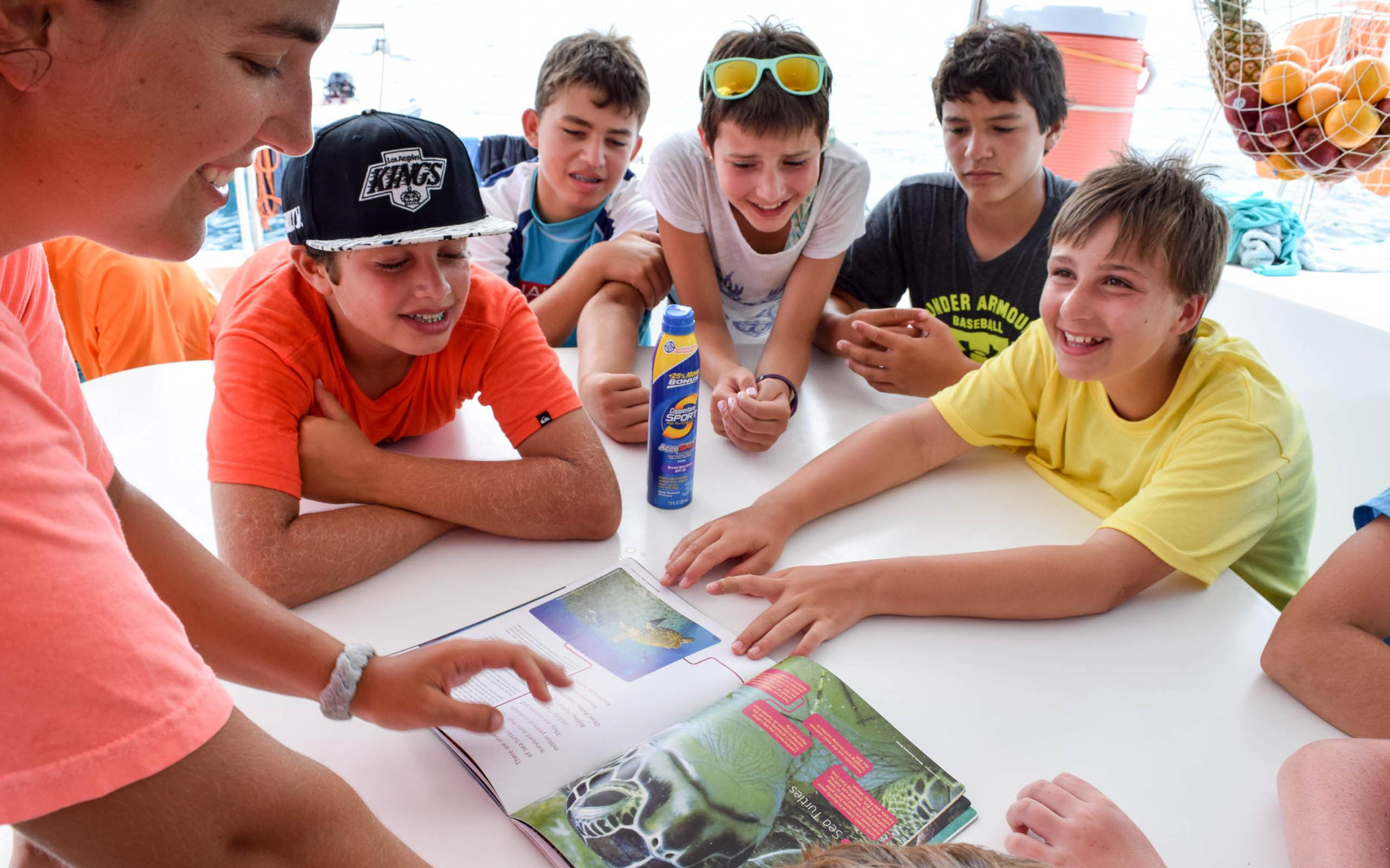 A group of kids sitting around a table looking at a book.