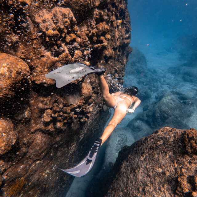 A woman snorkling in the water near a rock.