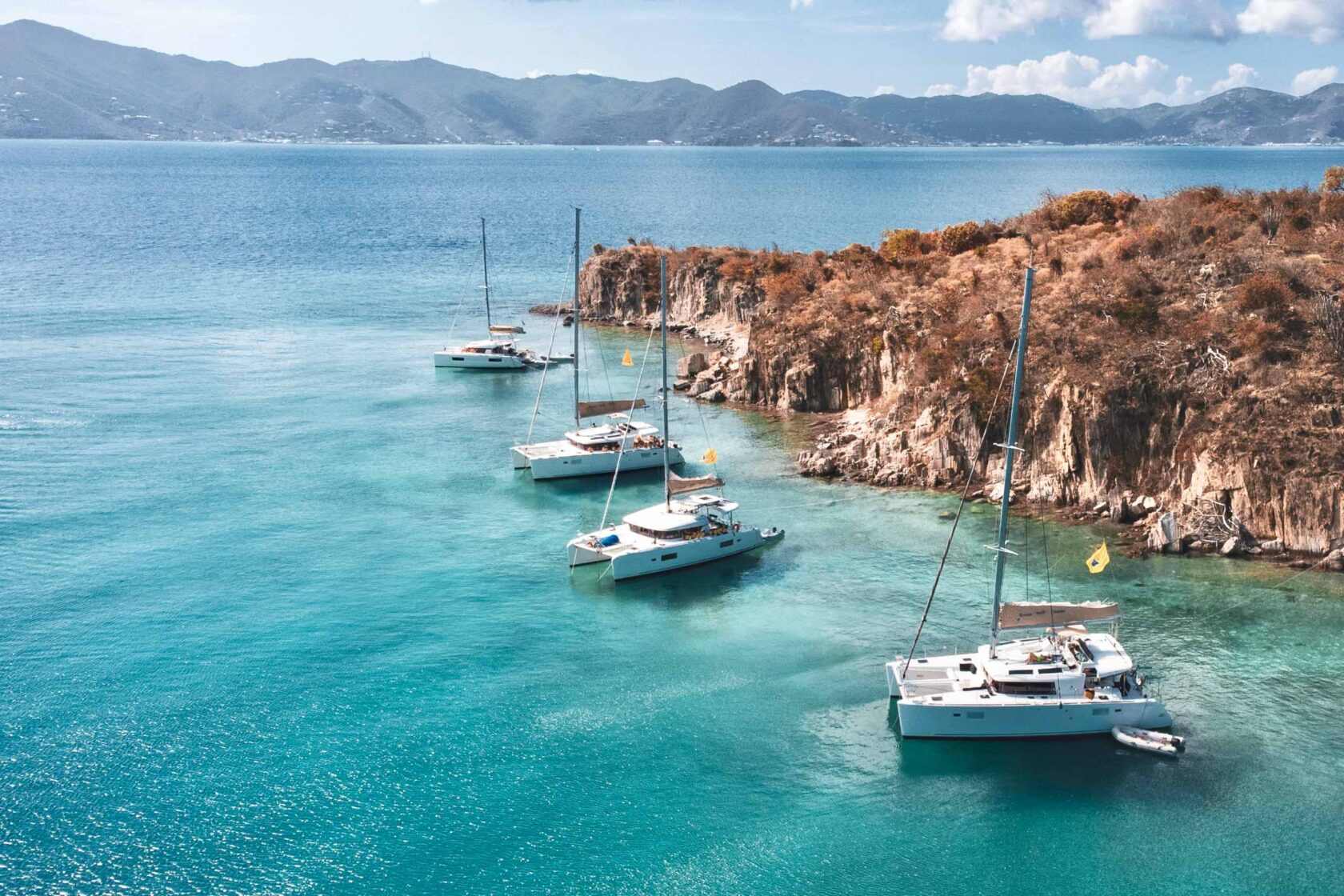 A group of sailboats docked in the water near a cliff.