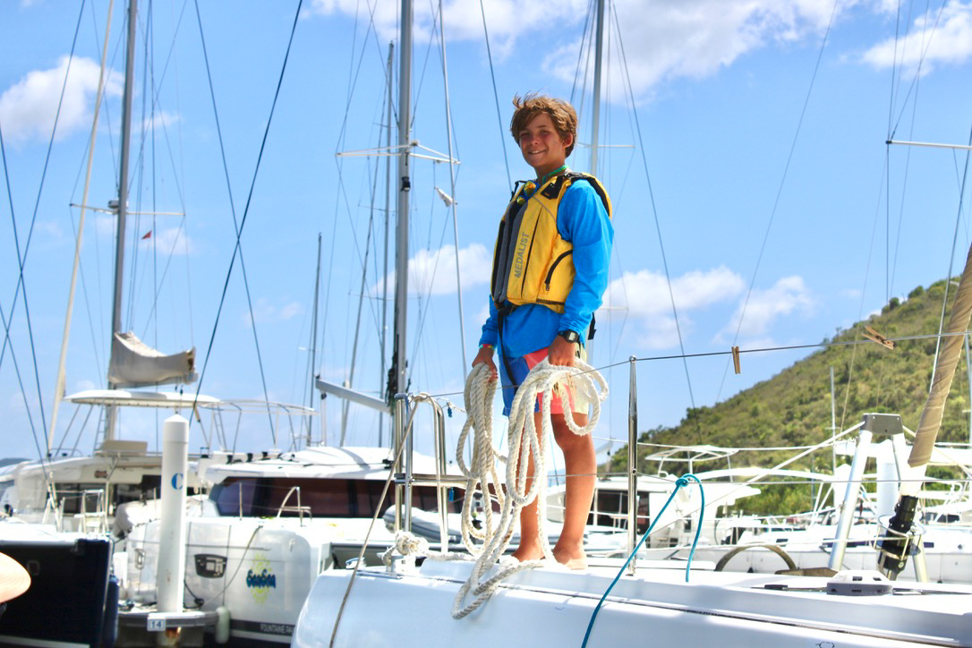 A young man standing on the top of a sailboat.