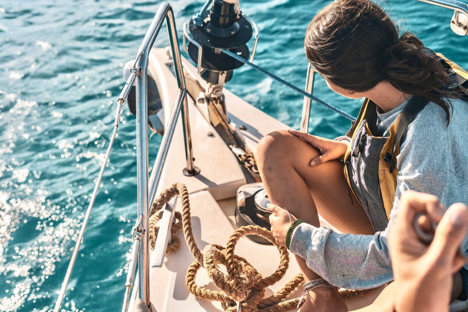 A woman is sitting on the back of a sailboat.